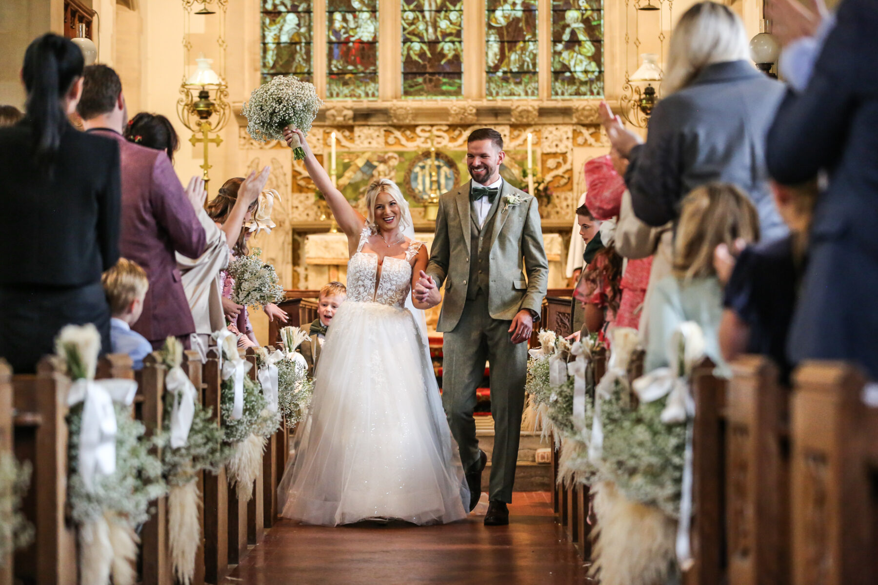 Bournemouth wedding photographer capturing bride and groom walking down church aisle after ceremony cheering guests