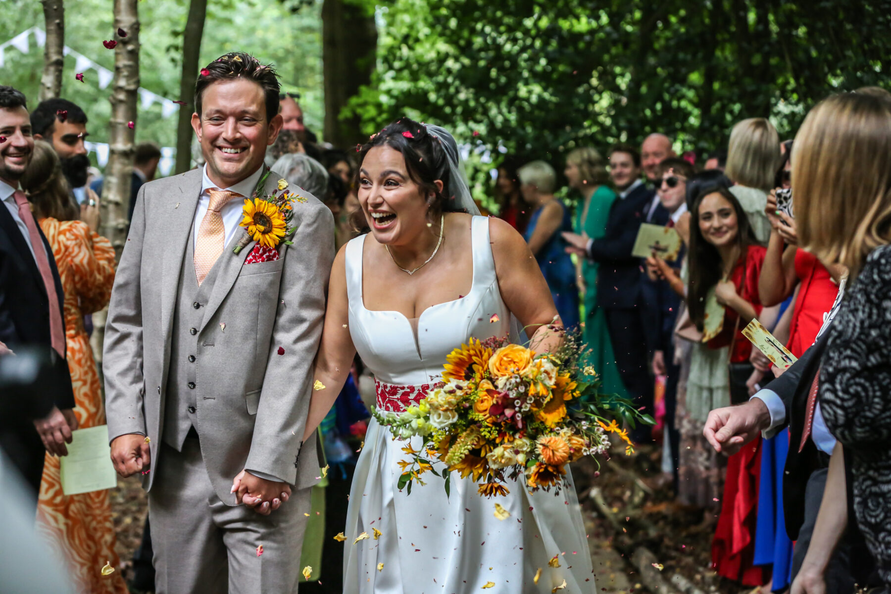 Bournemouth wedding photographer capturing joyful bride and groom walking through confetti after woodland ceremony