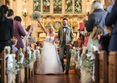 Bournemouth wedding photographer capturing bride and groom walking down church aisle after ceremony cheering guests