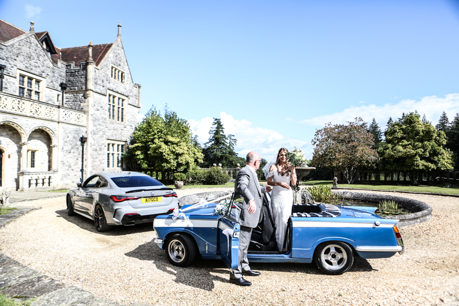 Bride stepping out of vintage car by the fountain pond at a Rhinefield House wedding in the New Forest