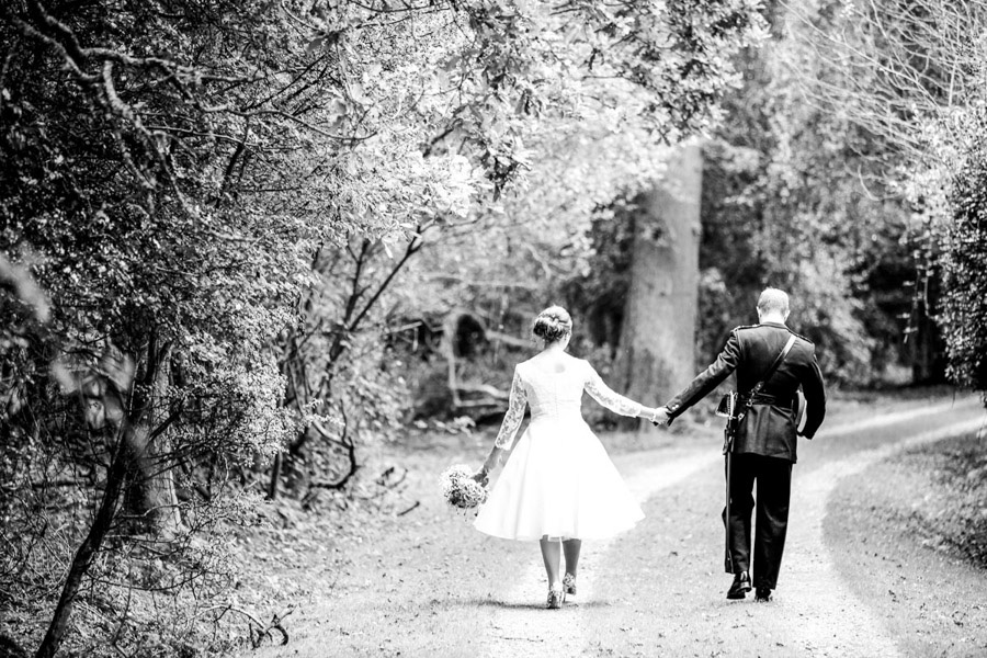 Bride and groom walking hand in hand along a tree lined path in Dorset captured by wedding photography and videography team